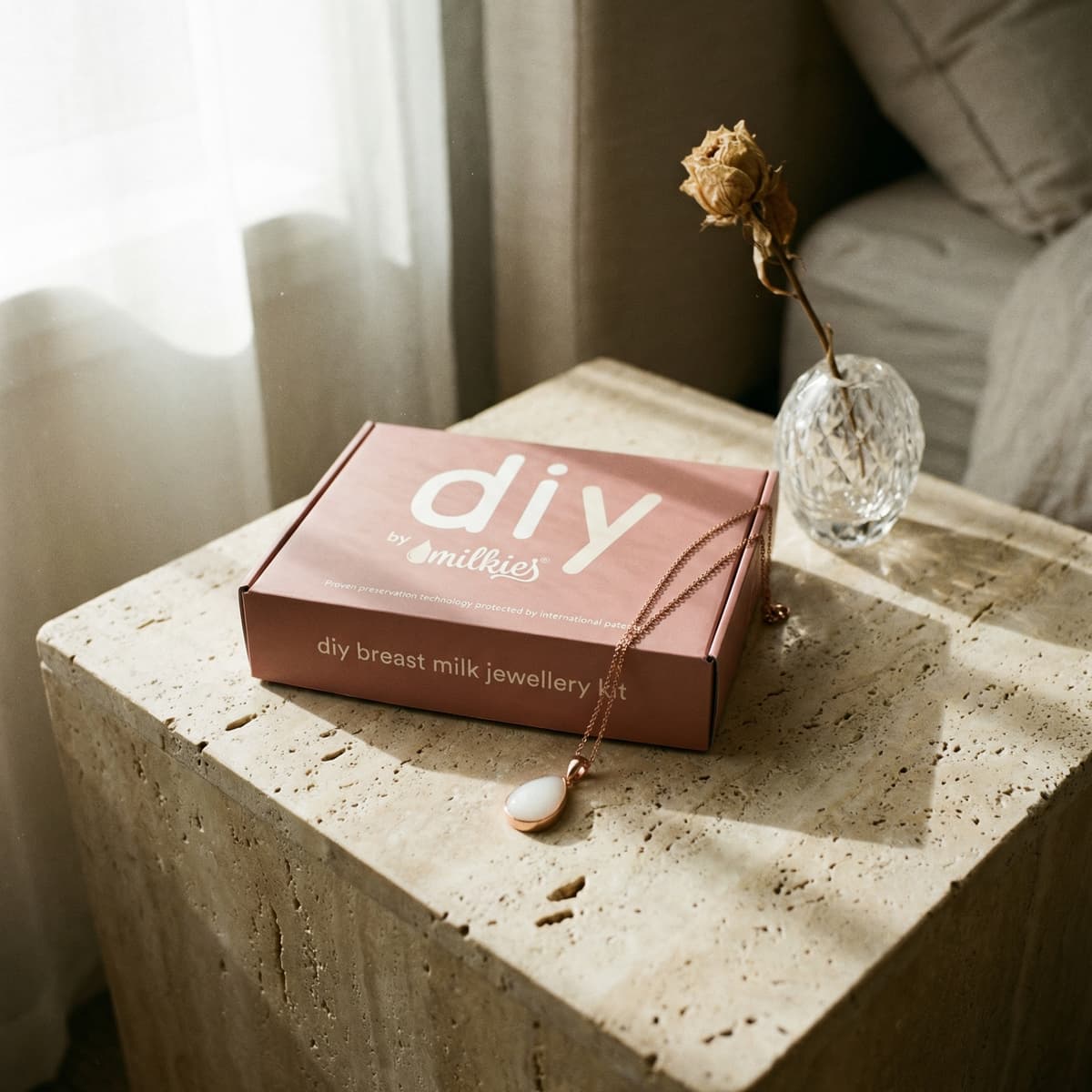 Elegancki zestaw DIY by MILKIES do tworzenia biżuterii z mleka mamy w pudełku, z delikatnym naszyjnikiem na kamiennym stoliku — wyjątkowy prezent za urodzenie dziecka.