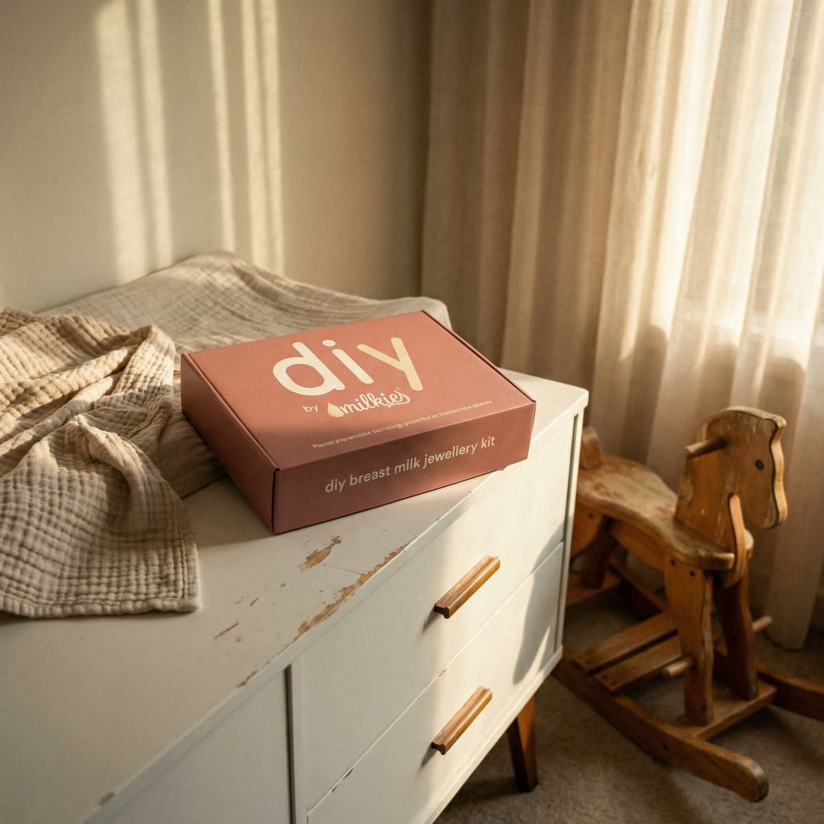 Estetyczne pudełko DIY by MILKIES z zestawem do tworzenia biżuterii z mleka mamy na białej komodzie w pokoju dziecięcym, jako wyjątkowy prezent dla kobiety w ciąży.