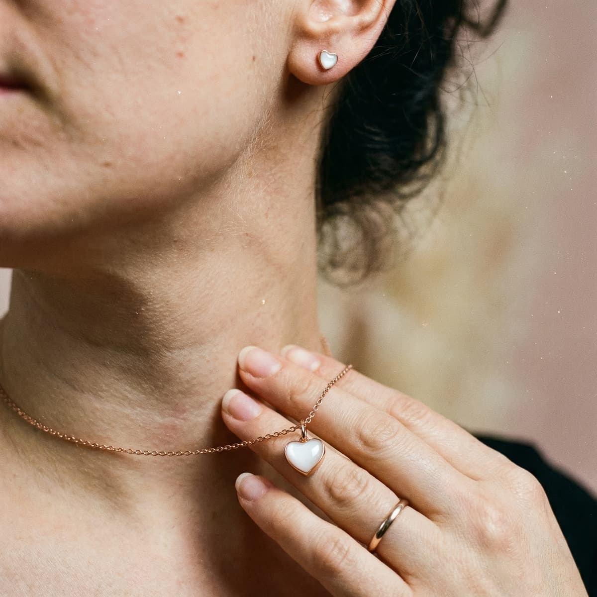 Zbliżenie na kobietę noszącą delikatny naszyjnik z serduszkiem w kolorze różowego złota i kolczyk, idealny jako prezent karmienie piersią dla mamy w formie biżuterii pamiątkowej.